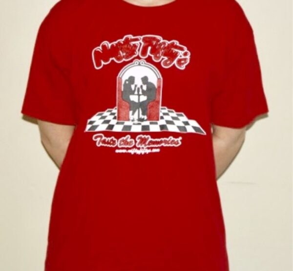 Person wearing a red T-shirt with a graphic of two people dancing in front of a jukebox on a checkered floor, and stylized text that reads “Make Magic” and “Twist the Memories.”.