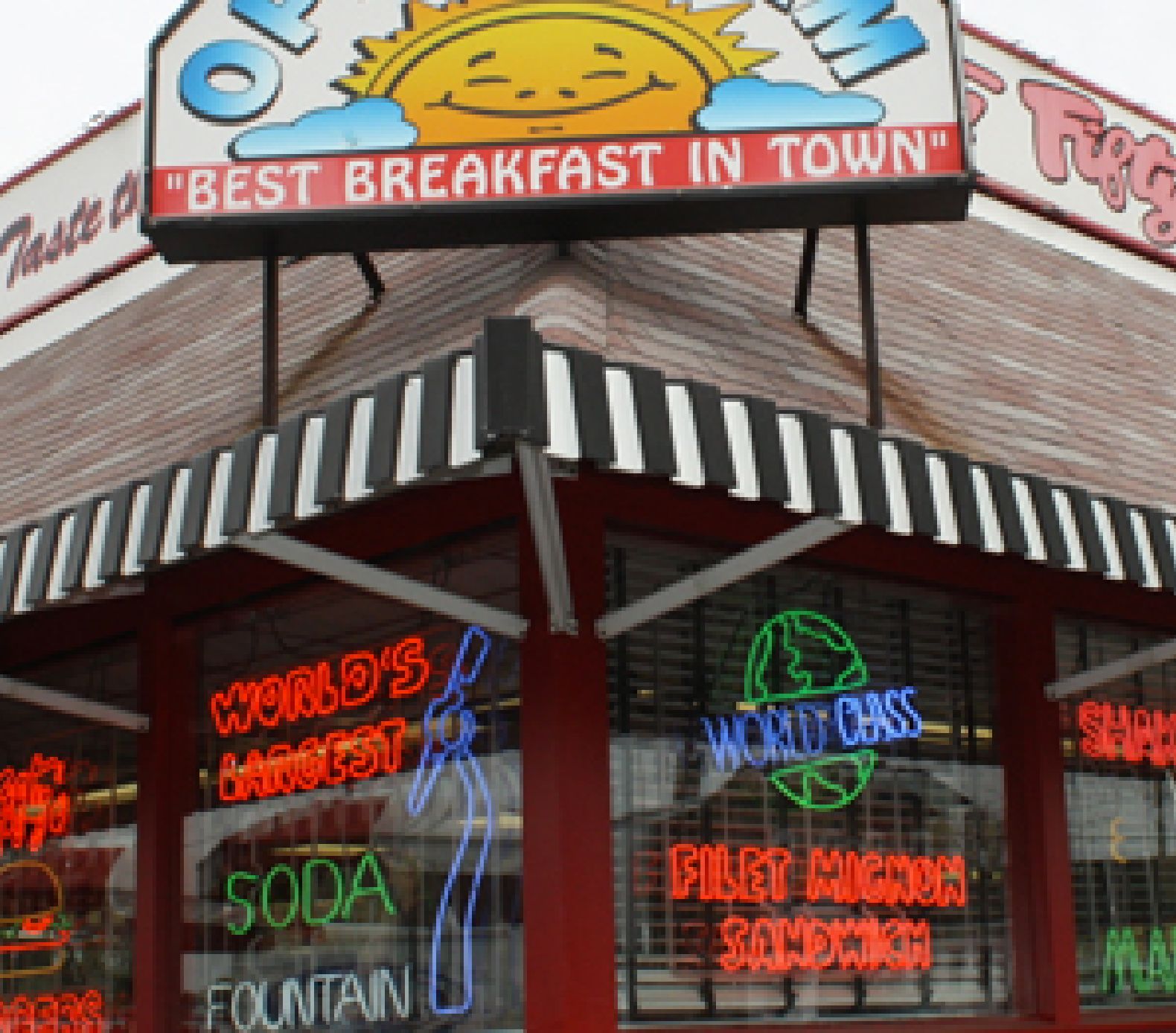Nifty Fifty's diner with a sign reading Best Breakfast in Town and neon signs in the windows advertising Worlds Largest Soda Fountain, World Class Filet Mignon Sandwich, and other menu items.